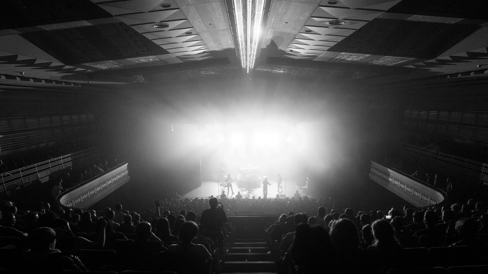 A black-and-white view across a packed theatre toward Enter Shikari on stage.