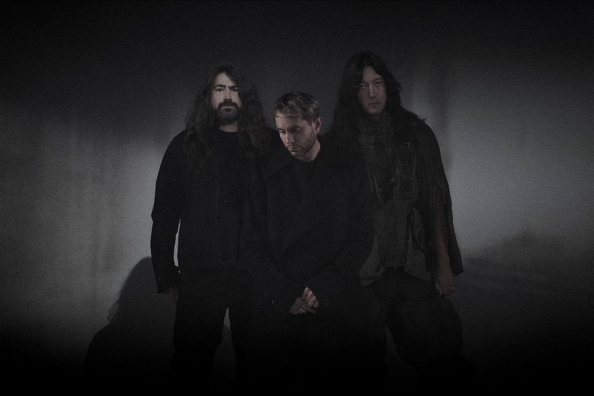The three members of HEALTH stand together against a dark studio backdrop.